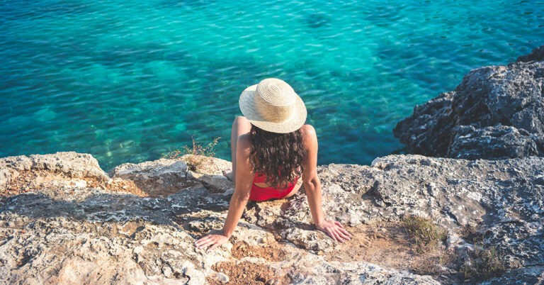 A girl in a red bikini and a hat is sunbathing on a cliff by the sea