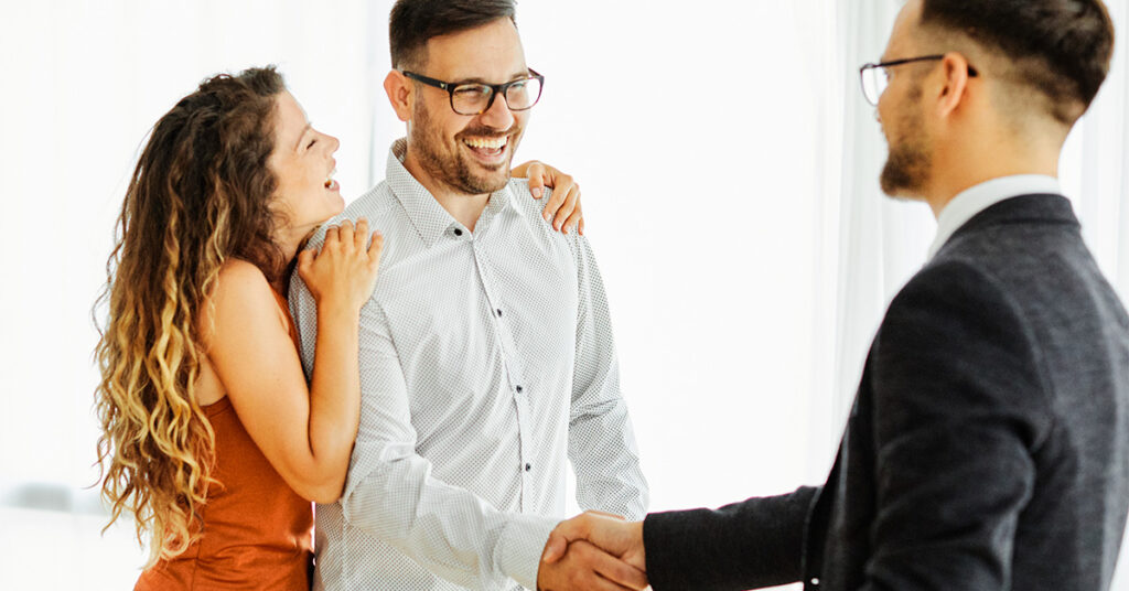 A man and a woman smile and shake hands with the agent.